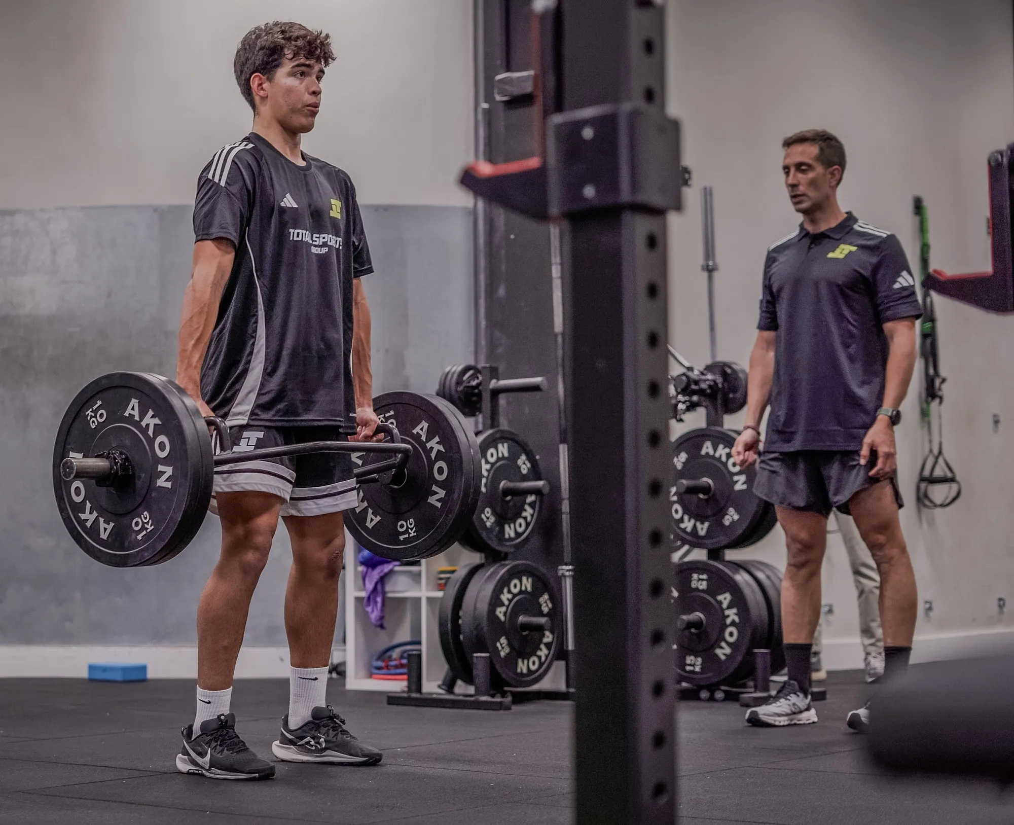 Un jugador levantando una barra cargada en el gimnasio con un entrenador supervisando